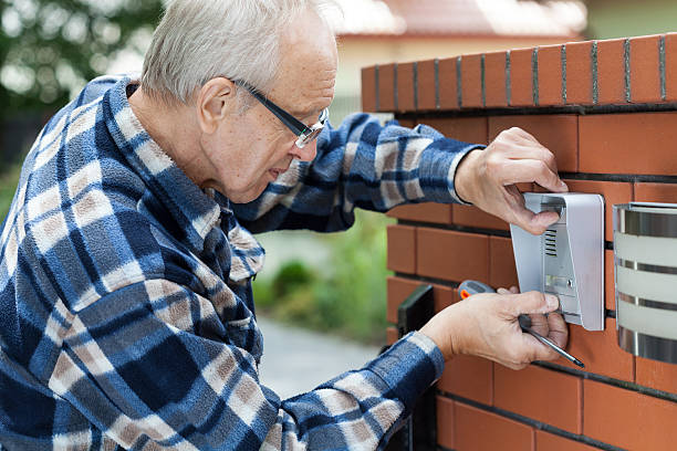 Handyman in flannel shirt fixing intercom, horizontal